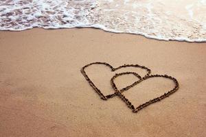 twee harten getekend in zand op een strand