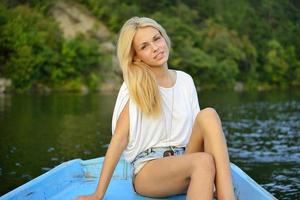 mooie jonge blonde zittend in een boot en zachtjes glimlachen foto