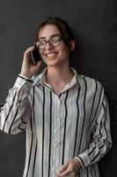 opstarten zakenvrouw in overhemd met een bril gebruik makend van smartphone terwijl staand in voorkant van grijs muur gedurende breken van werk buiten foto
