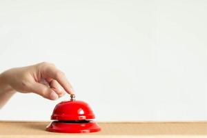 detailopname van inhoudsopgave vinger drukken de klok knop van rood wijnoogst stijl tafelbel Aan houten tafel. foto