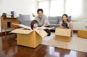 Aziatisch familie man en vrouw en kinderen met karton dozen hebben pret Aan in beweging dag, hypotheek, lening, eigendom en verzekering concept. foto