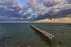 oud gebroken brug in de zee Bij bewolkt zonsondergang foto