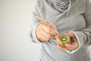 jonge vrouw die rijpe kiwi's eet met houten lepel foto