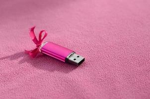 briljant roze USB flash geheugen kaart met een roze boog leugens Aan een deken van zacht en harig licht roze fleece kleding stof. klassiek vrouw geschenk ontwerp voor een geheugen kaart foto