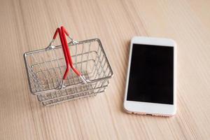 mobiel telefoon met mand Aan hout tafel achtergrond boodschappen doen online concept foto