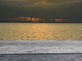 oud houten tafel plank in de achtergrond landschap een meer met zwart regen wolken en oranje balken. foto