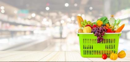 winkelmandje gevuld met fruit en groenten op houten tafel met supermarkt supermarkt wazig onscherpe achtergrond met bokeh licht foto