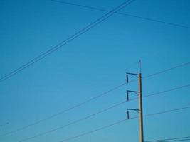 de hoog Spanning licht pool vastgemaakt naar meerdere draden leidend naar Aan de achtergrond is een blauw lucht foto