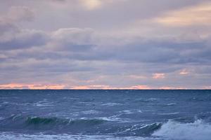 paarse bewolkte lucht en blauwe zee met schuimende golven, zeegezicht foto