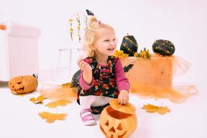 grappig en schattig weinig blond kromme meisje met pompoen in halloween decoratie foto