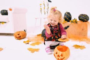 grappig en schattig weinig blond kromme meisje met pompoen in halloween decoratie foto