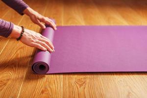 een meisje legt uit een lila yoga mat voordat een training praktijk Bij huis Aan een houten vloer. foto