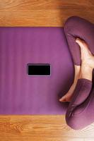 een meisje doet yoga met een smartphone online via de internet Aan een lila tapijt in de leven kamer foto