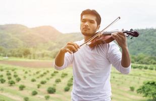 jonge hipster muzikant man viool spelen in de natuur buiten levensstijl achter de berg. foto