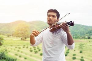 jonge hipster muzikant man viool spelen in de natuur buiten levensstijl achter de berg. foto