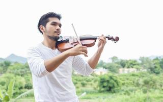 jonge hipster muzikant man viool spelen in de natuur buiten levensstijl achter de berg. foto