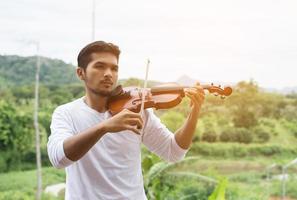 jonge hipster muzikant man viool spelen in de natuur buiten levensstijl achter de berg. foto