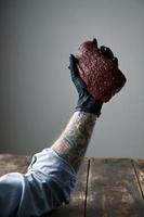 De getatoeëerde zwarte siliconenhandschoen voor de linkerhand houdt vers walvisvlees vast