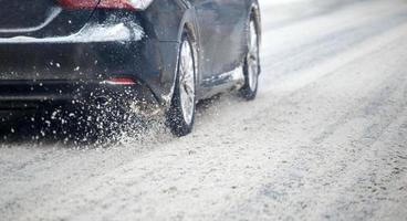 weg sneeuw flinders stromen van wielen van zwart auto in beweging snel in daglicht stad met selectief focus. foto