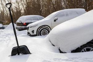 groot zwart plastic Schep in de buurt sneeuw gedekt auto's Bij winter dag licht na zwaar sneeuwval foto