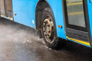 blauw gemeentelijk bus in beweging Aan regenachtig weg met water spatten foto