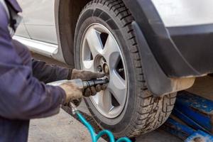 handen van automotive monteur losschroeven noten met pneumatisch gevolg moersleutel gedurende auto wielen seizoen veranderen foto