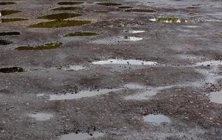 hobbelig beschadigd weg asfalt met meerdere plassen na regen Bij zomer dag foto