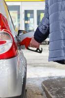 oud Mens hand- in blauw warm jasje tanken grijs metalen auto Aan gas- station Bij dag tijd - detailopname met selectief focus foto