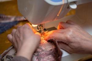 een detailopname visie van naaien werkwijze, hand- van oud vrouw gebruik makend van naaien machine, selectief focus techniek foto