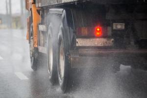 regen water plons stromen van wielen van zwaar vrachtauto in beweging snel in daglicht stad met selectief focus. foto