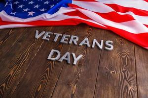 de woorden veteranen dag gelegd met zilver metaal brieven Aan houten bord oppervlakte met verfrommeld Verenigde Staten van Amerika vlag foto