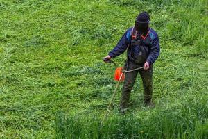 grasmaaier Mens met draad trimmer en gezicht masker bijsnijden gras - detailopname foto