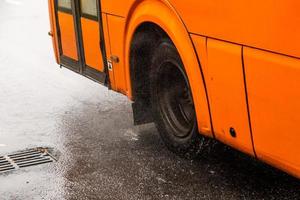 oranje gemeentelijk bus in beweging Aan regenachtig weg met water spatten foto