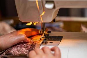 een detailopname visie van naaien werkwijze, hand- van oud vrouw gebruik makend van naaien machine, selectief focus techniek foto