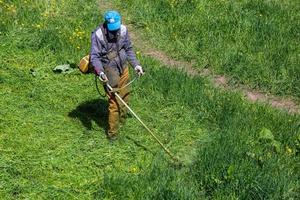 tula, Rusland mei 19, 2020 Russisch officieel grasmaaier arbeider Mens snijdend groen gras met twee-cyclus motor draad trimmer. top naar naar beneden visie. foto