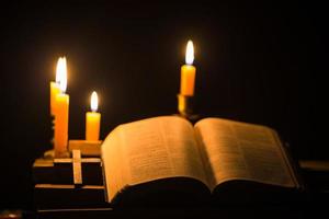 licht kaars met heilig Bijbel en kruis of kruisbeeld Aan oud houten achtergrond in kerk.kaarslicht en Open boek Aan wijnoogst hout tafel Christendom studie en lezing in home.concept van Christus religie foto