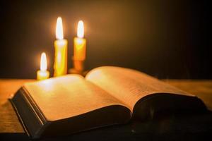 licht kaars met heilig Bijbel en kruis of kruisbeeld Aan oud houten achtergrond in kerk.kaarslicht en Open boek Aan wijnoogst hout tafel Christendom studie en lezing in home.concept van Christus religie foto