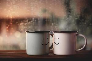liefde en valentijnsdag dag concept. paar van koffie kop met glimlachen gezicht door glas venster in huis. geluk, romantisch of positief geest Aan regenachtig dag foto