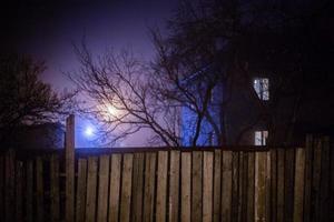 donker mistig nacht visie Aan houten hek en spookachtig huis met sel foto