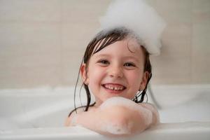 weinig meisje in bad spelen met schuim foto