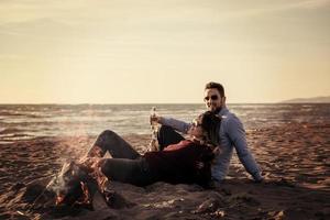 jong paar zittend Aan de strand naast kampvuur drinken bier foto