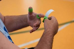 een gehandicapt basketbal speler zet Aan een korset en verbanden Aan zijn armen en vingers in voorbereiding voor een spel in de arena foto