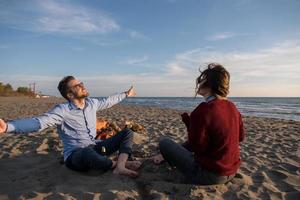 jong paar zittend Aan de strand naast kampvuur drinken bier foto