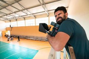 een cameraman met professioneel uitrusting records een bij elkaar passen van de nationaal team in een rolstoel spelen een bij elkaar passen in de arena foto