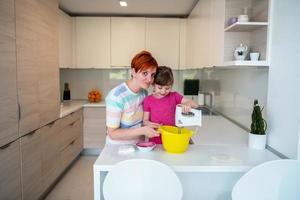 grappig weinig meisje helper spelen met deeg Aan zijn handen aan het leren naar kneden helpt volwassen mam in de keuken, gelukkig schattig baby dochter en ouder mam hebben pret Koken koekjes. foto