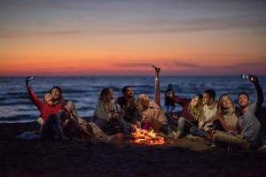 een groep van vrienden genieten van vreugdevuur Aan strand foto