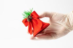 een rood klok gehouden in een hand- in een beschermend handschoen Aan een wit achtergrond. symbool van de vakantie gedurende een pandemie. plaats voor tekst. foto