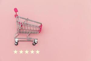 kleine supermarkt kruidenierswinkel duwkar voor winkelen speelgoed met wielen en 5 sterren geïsoleerd op pastel roze achtergrond. retailconsument die online beoordelings- en beoordelingsconcept koopt. foto