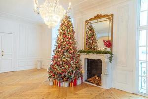 klassiek Kerstmis versierd interieur kamer, nieuw jaar boom met rood en goud decoraties. modern wit klassiek stijl interieur ontwerp appartement met haard en Kerstmis boom. Kerstmis vooravond Bij huis. foto