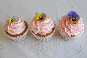 zelfgemaakte roze frosting vanille cupcakes met eetbare bloemen foto